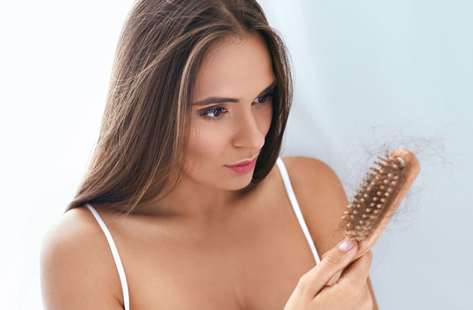 Mulher jovem segurando escova de cabelo cheia de cabelo
